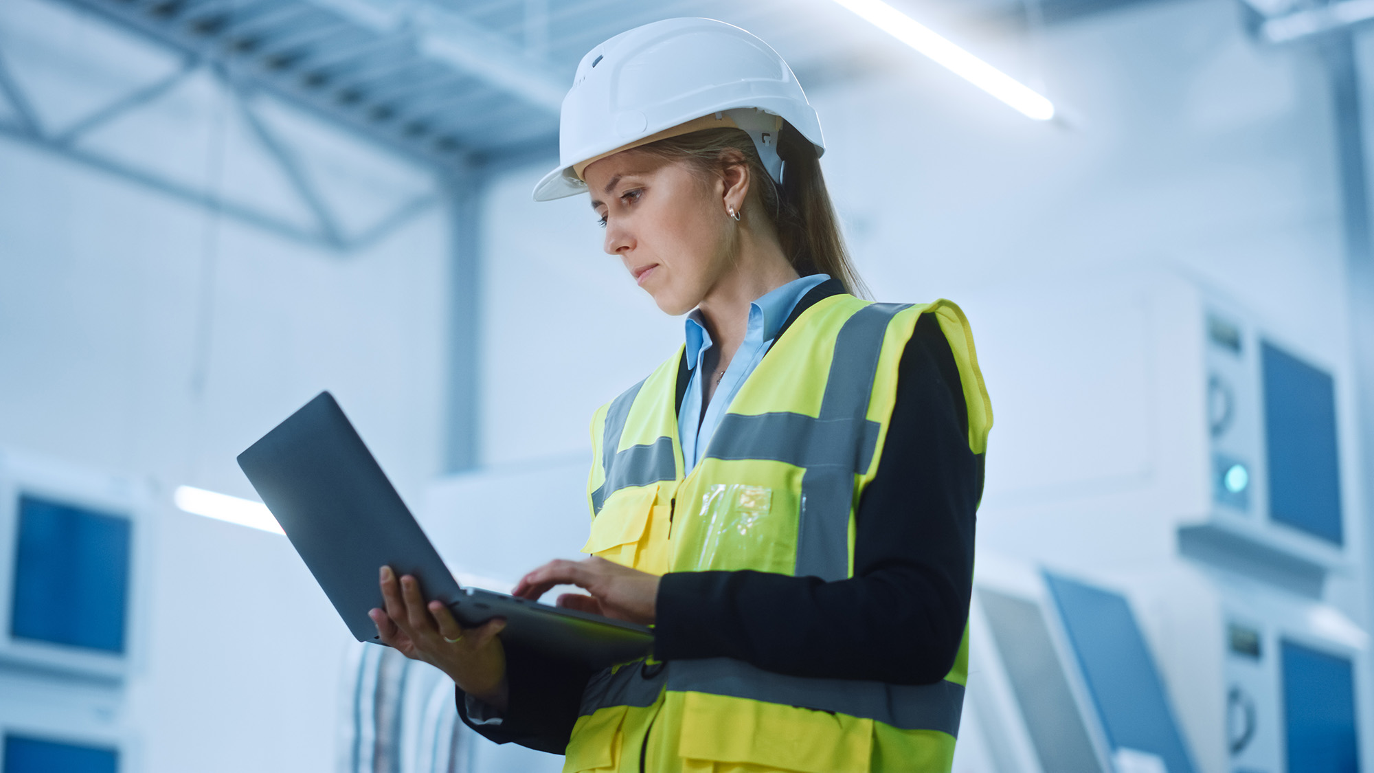 Ingenjör i varselväst med laptop i fabrik
